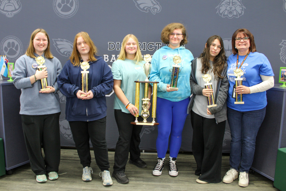 five middle school students and one teacher stand on stage for Battle of the Books championship holding trophies
