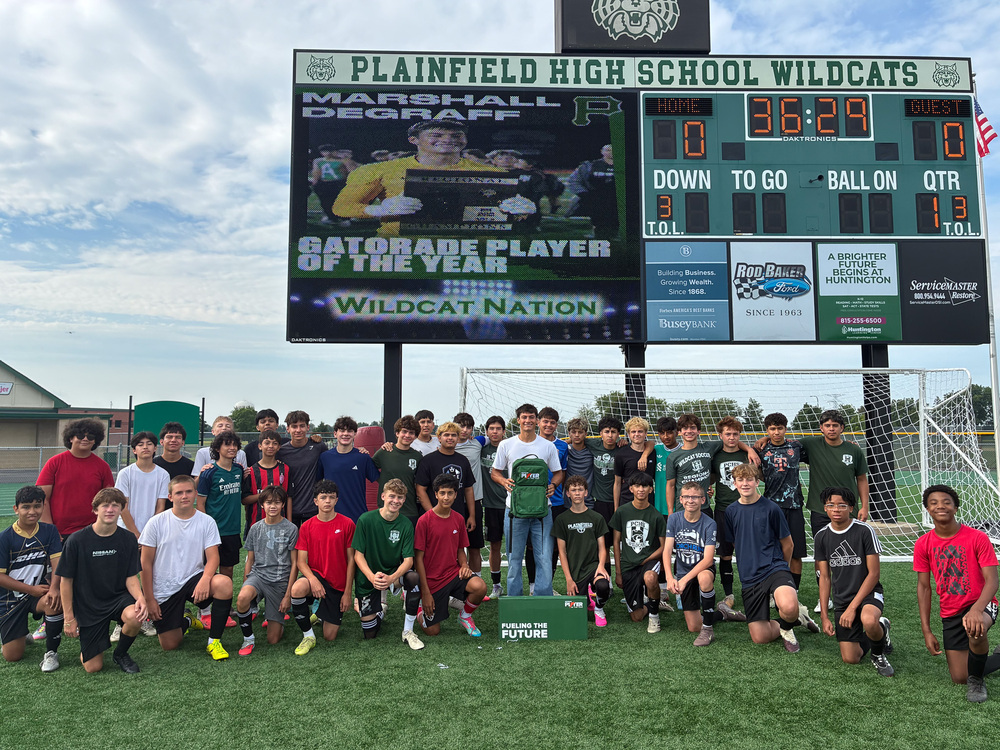group of high school soccer players stand in front of scoreboard