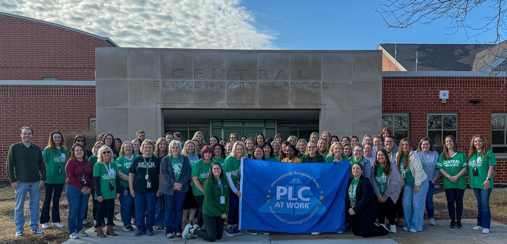group of people holding PLC At Work blue flag in front of Central Elementary School