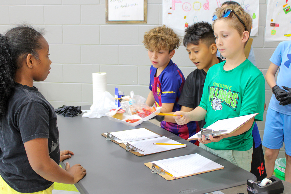 elementary school student hands lunch waste to three fifth graders one holding clipboard