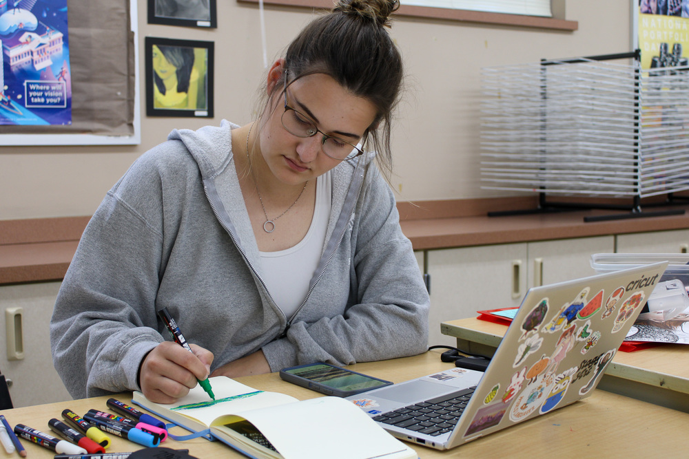 teacher drawing on sketch pad near open laptop