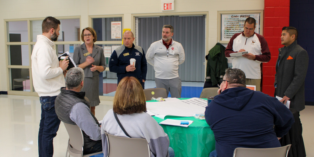 group of adults stand around and sit at table in cafeteria