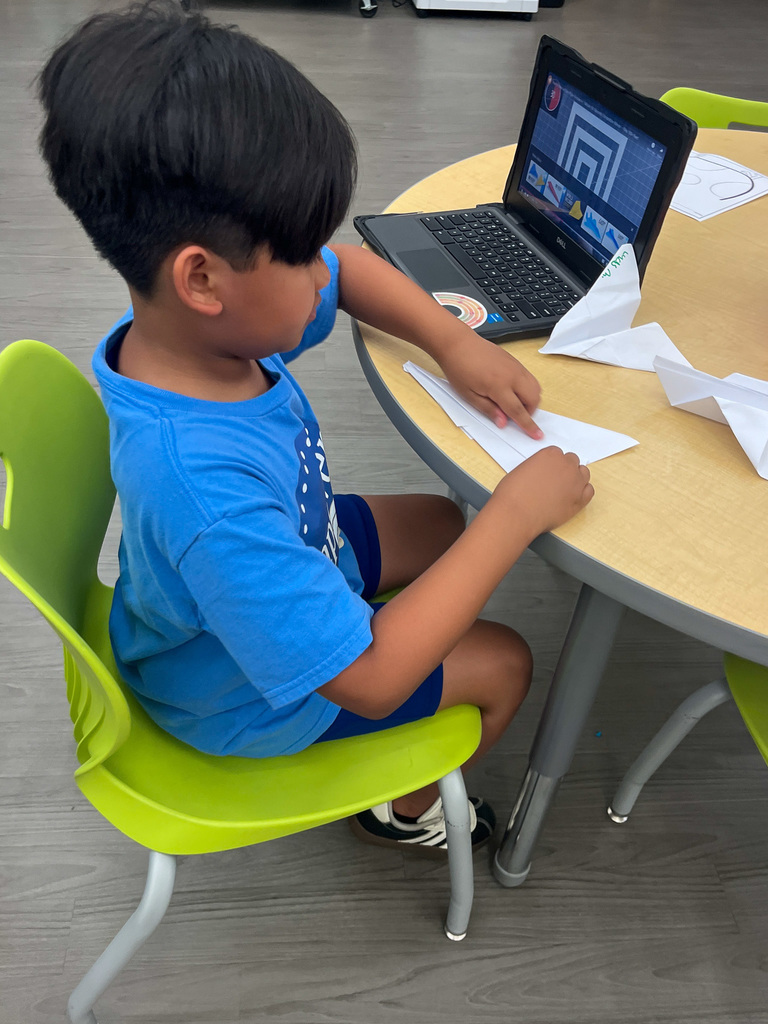 elementary school student sits at table making an paper airplane