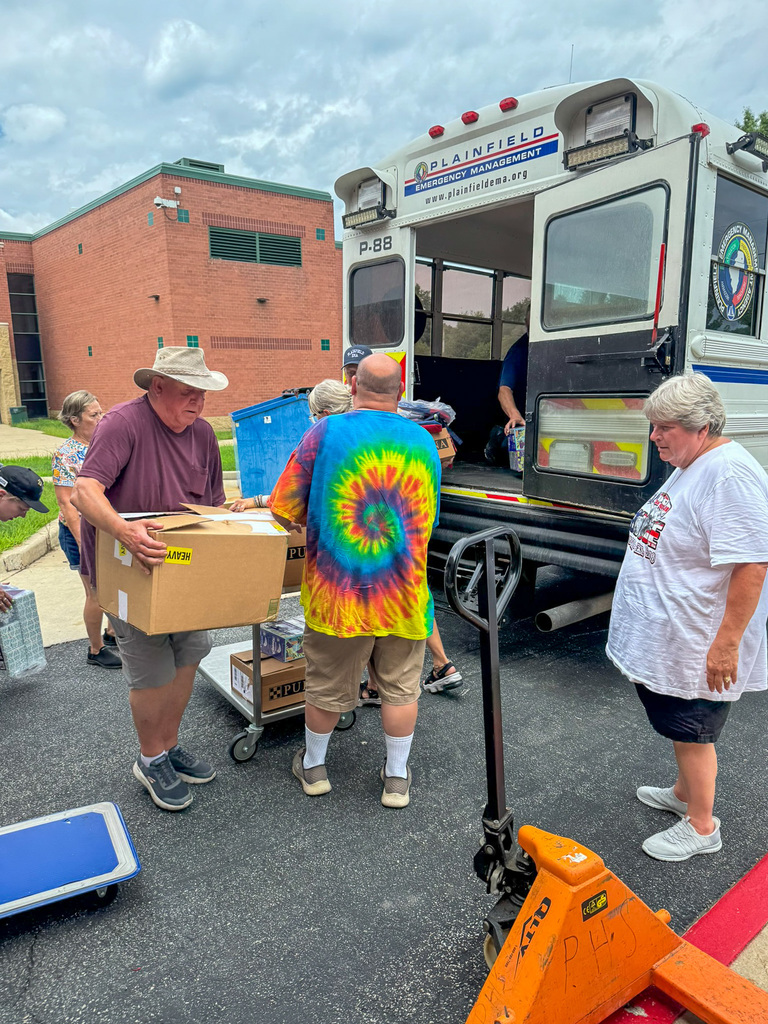 several adults unload boxes of school supplies from small bus
