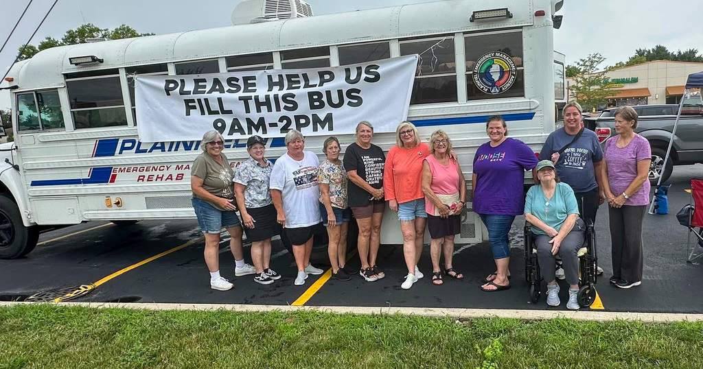 group of woman stand in side of bus with banner on it Please help us fill this bus 9 am - 2 pm