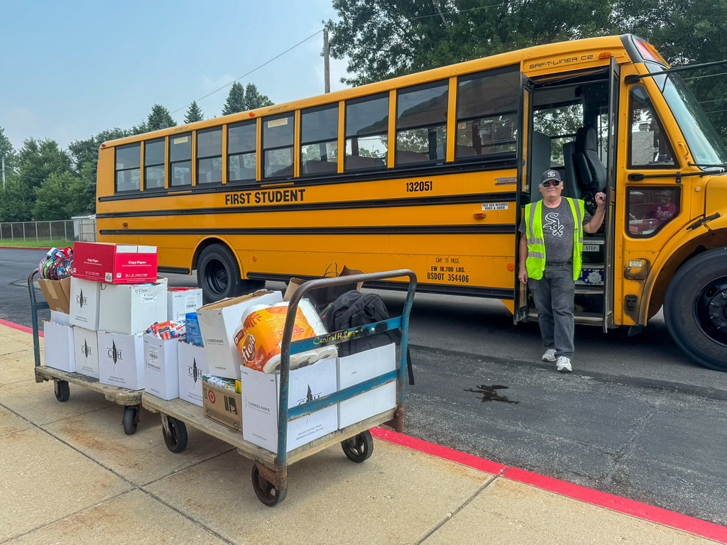 First student bus driver stands with bus and two carts full of donated school supplies