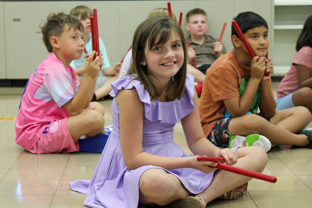 girl in purple dress smile while holding rhythm sticks in music class