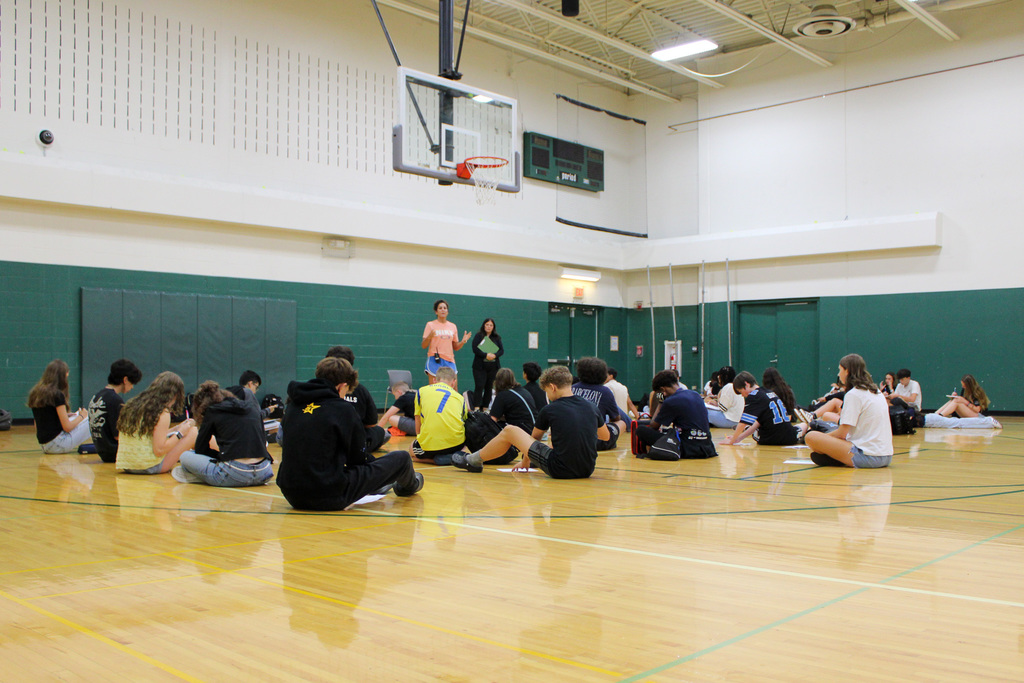 group of students sit on gym floor