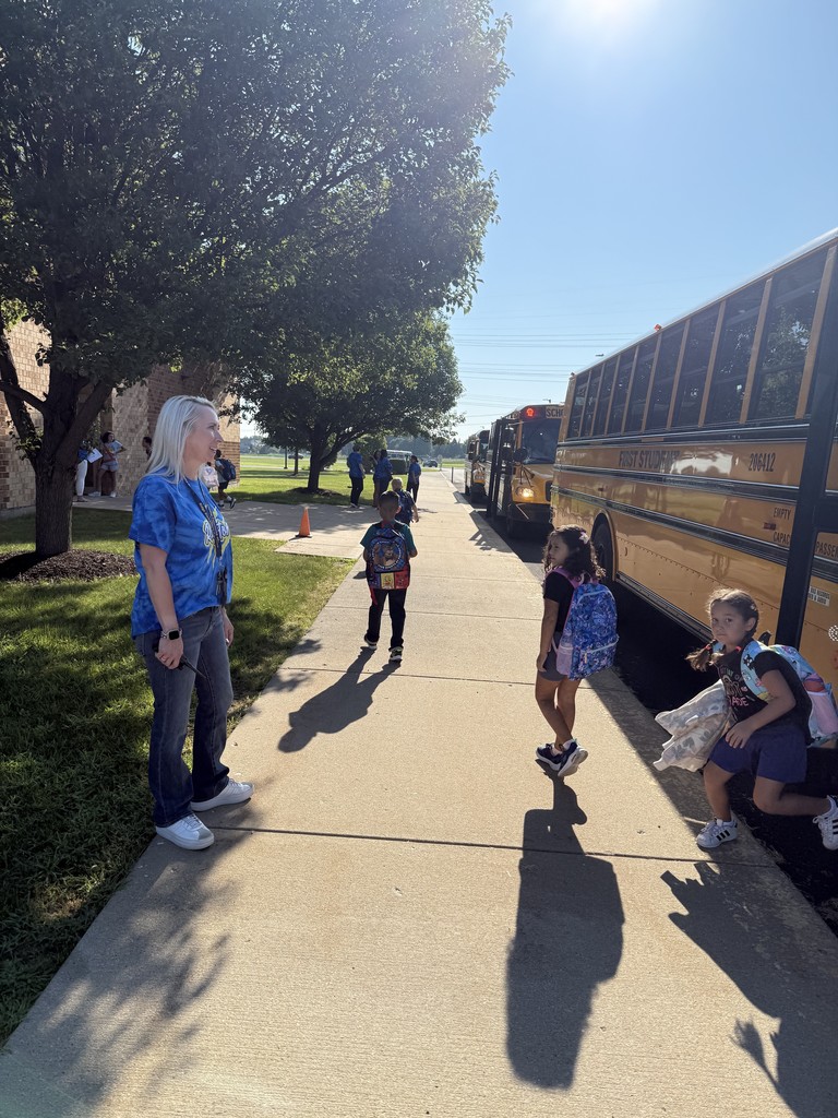 adults greet students as they get off the bus