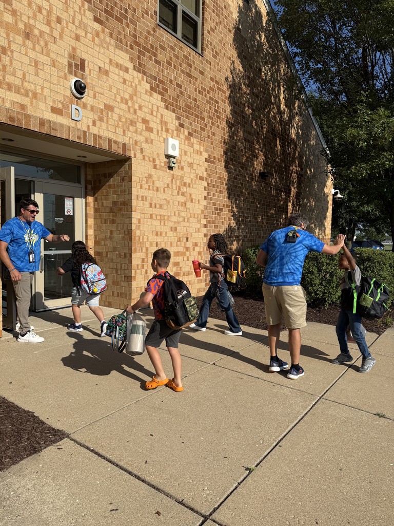 teachers and staff greet students as they enter school