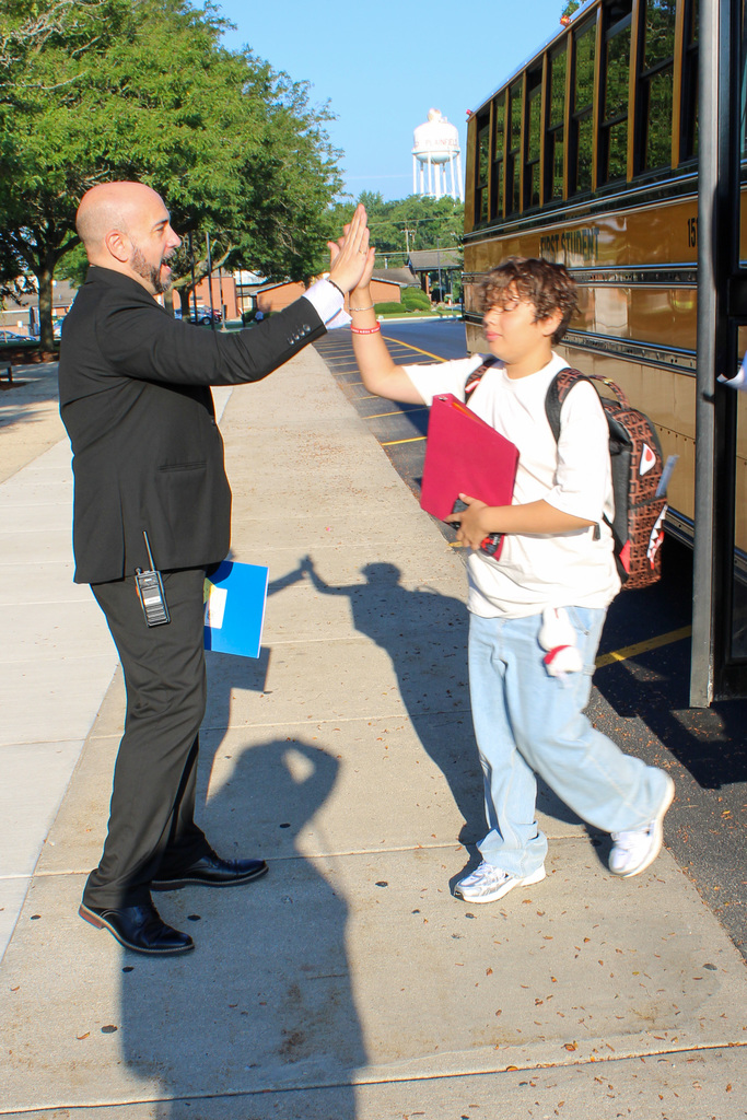 principal gives a high five to student getting off bus