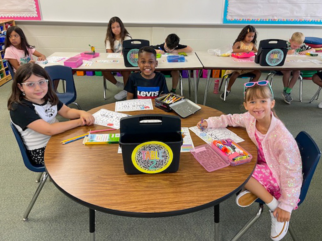 three students sit at round table coloring