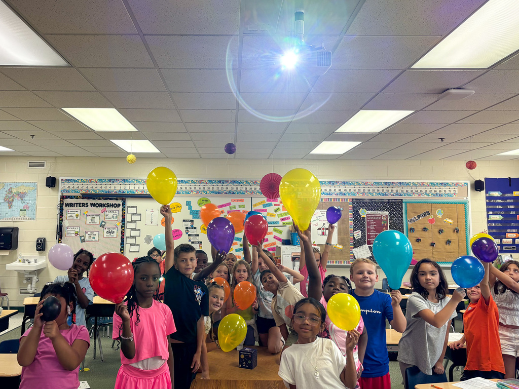 group of students hold up balloons in classroom