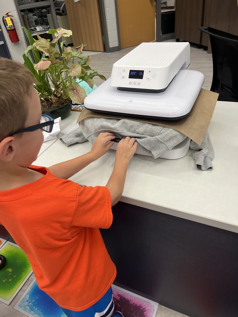 A student pushes  a sweatshirt under a press to create a custom hoodie. 