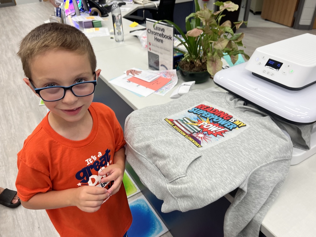 A student is standing in front of a press with a sweatshirt that has a decal on it that says reading is my superpower.