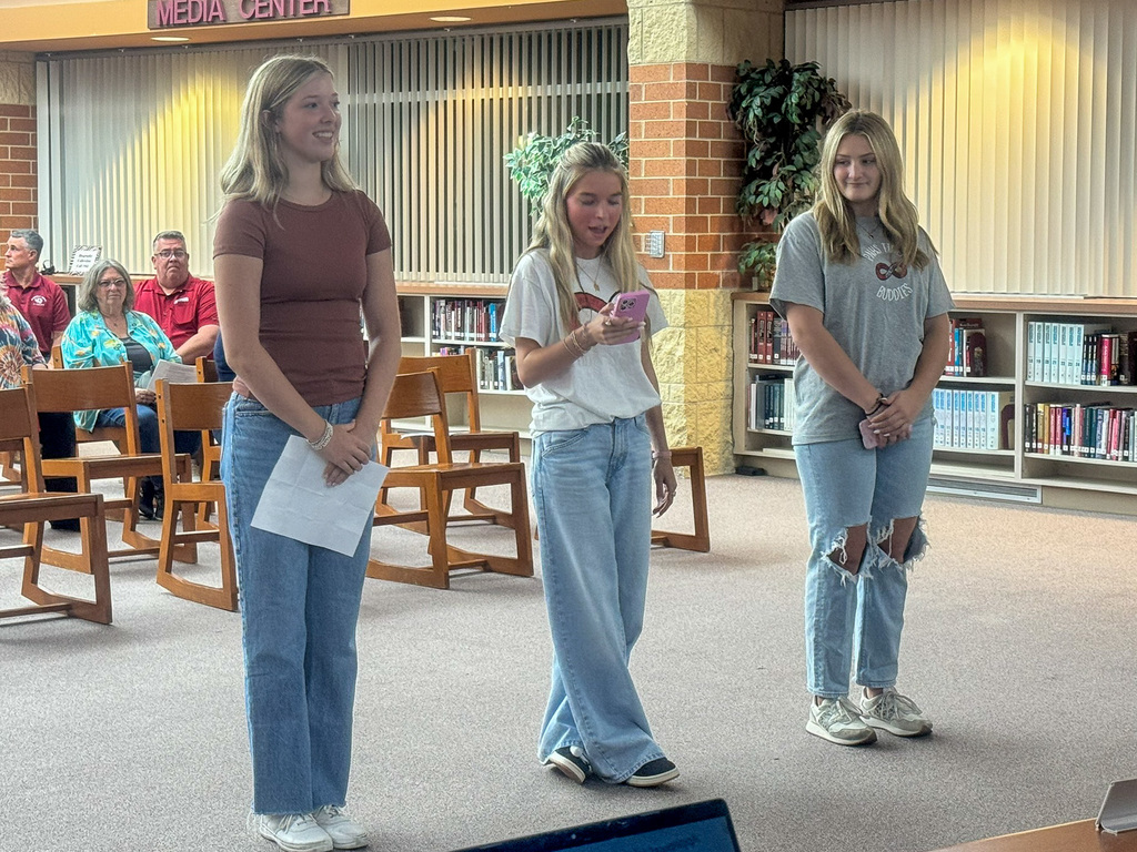 Three students stand in front of the school board and speak