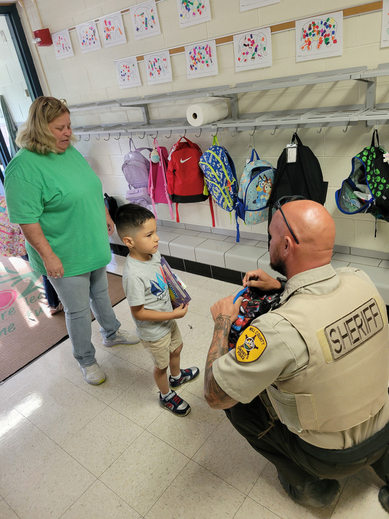 Will County Sheriff's Deputy crouches to talk to a student while teacher stands behind the student