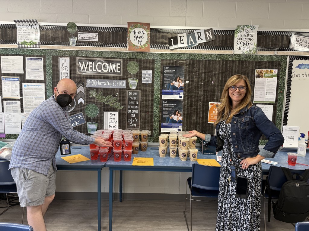 Two teachers standing in front of a table with 100 coffees.