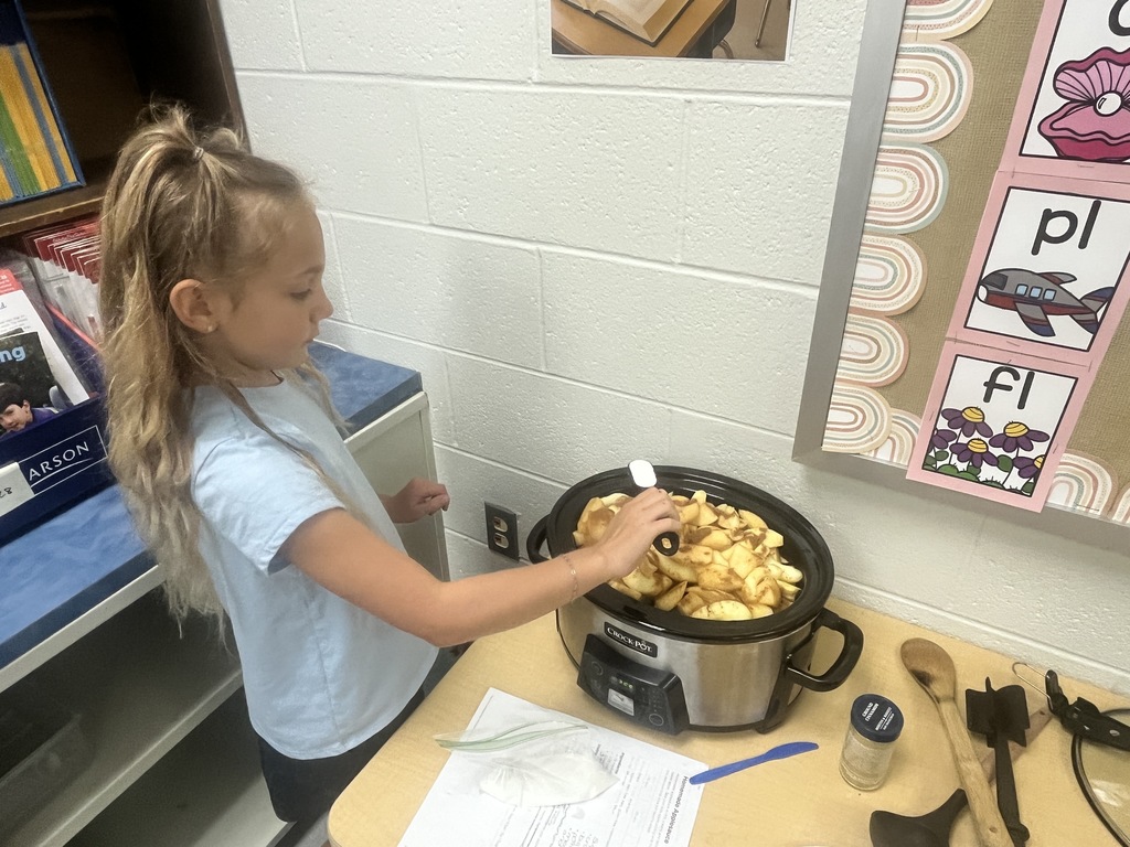 A student is stirring applesauce in a crockpot. 
