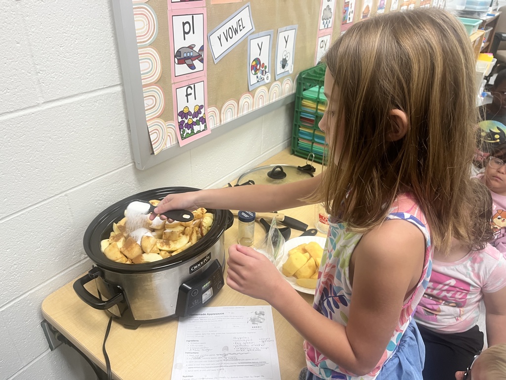 A student is stirring applesauce in a crockpot. 
