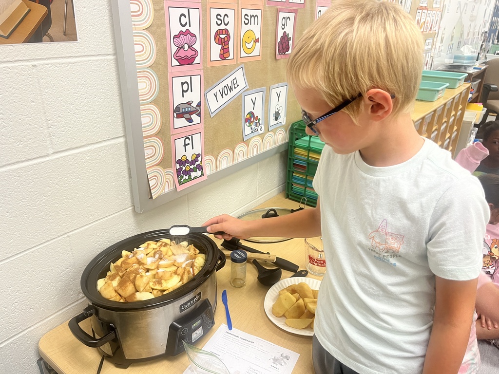 A student is stirring applesauce in a crockpot. 