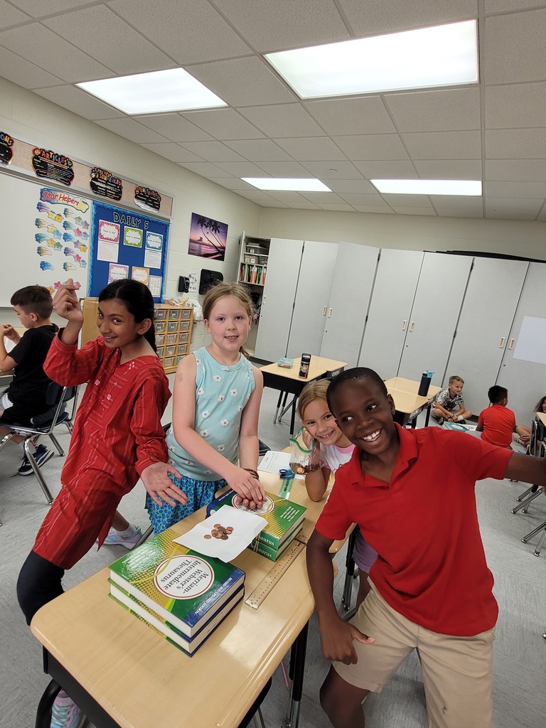 Four students building a bridge with books, paper, and pennies. 