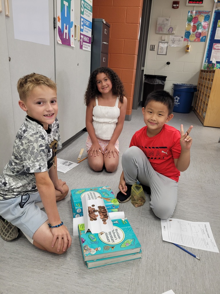 Three students building a bridge with books, paper, and pennies. 