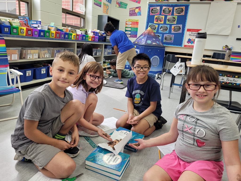 Four students building a bridge with books, paper, and pennies. 