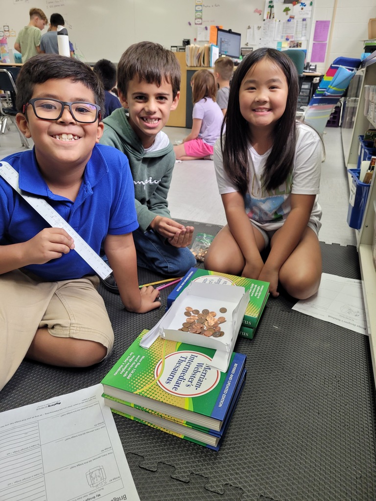 Three students building a bridge with books, paper, and pennies. 