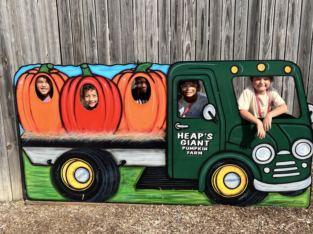 Five students posing behind a truck, hauling pumpkins. 