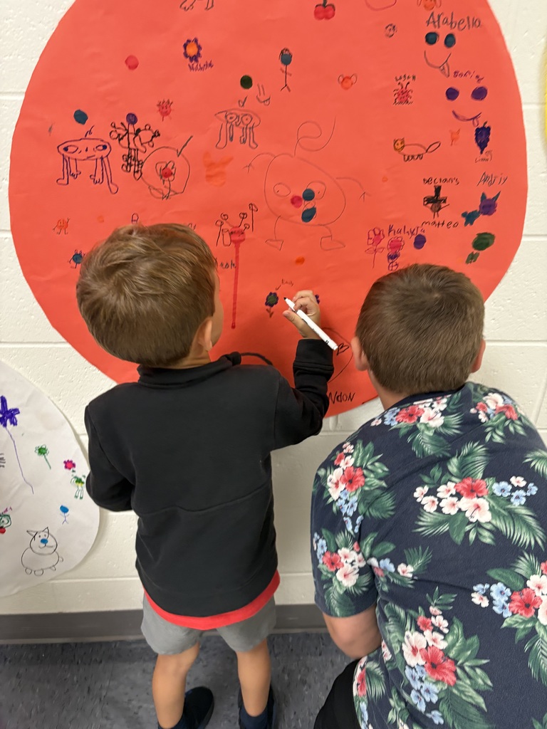 Two students are drawing on a circular shaped paper in a hallway. 