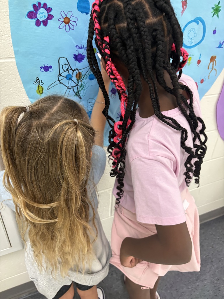 Two students are drawing on a circular shaped paper in a hallway. 
