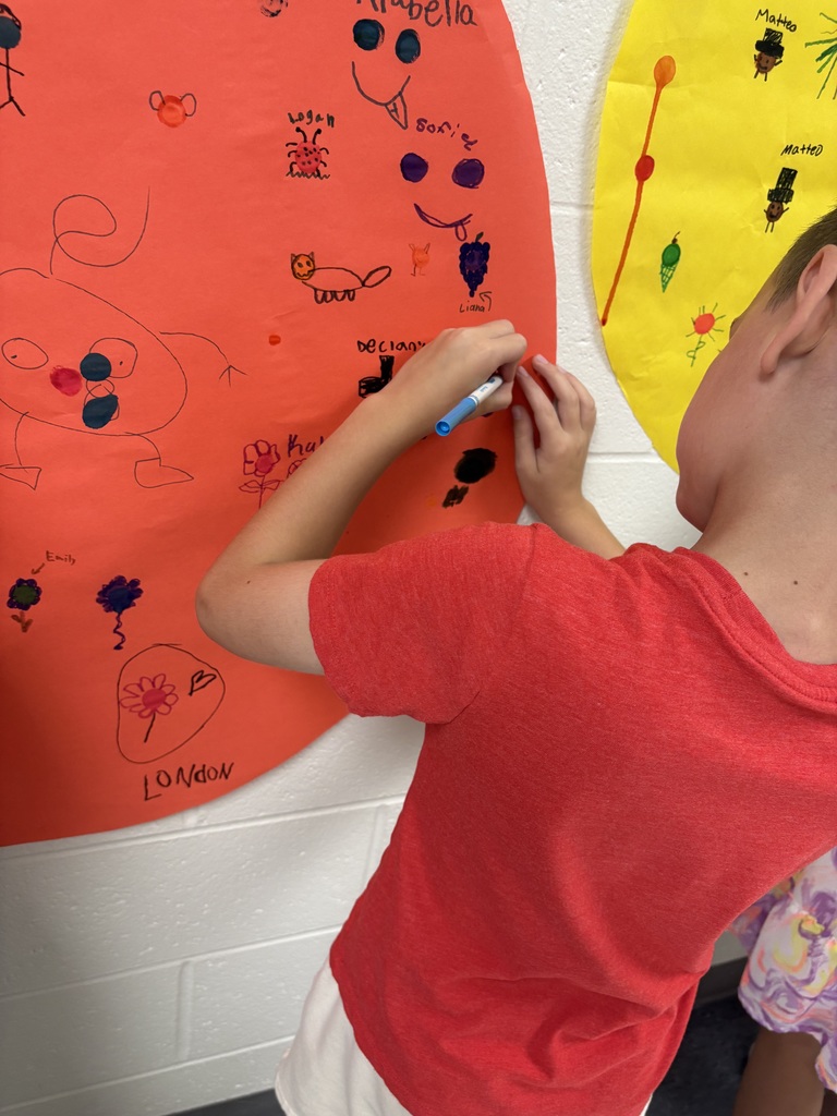 One student are drawing on a circular shaped paper in a hallway. 
