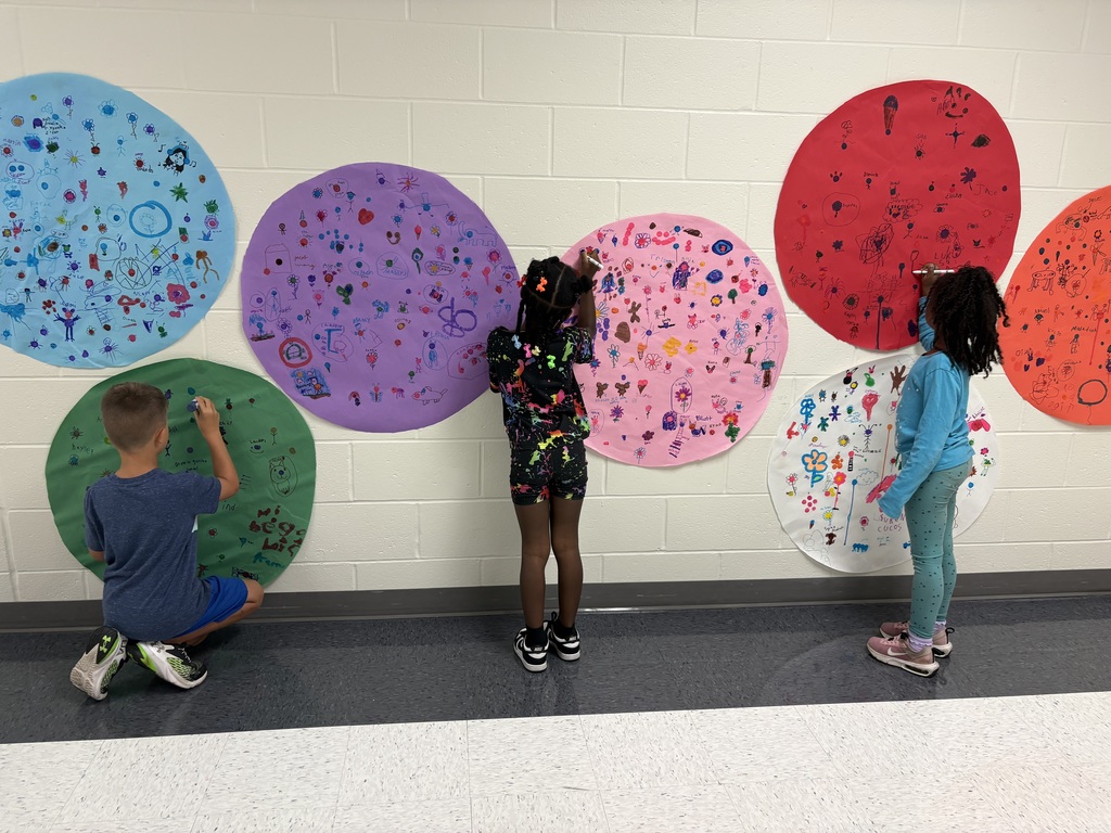 Three students are drawing on a circular shaped paper in a hallway. 