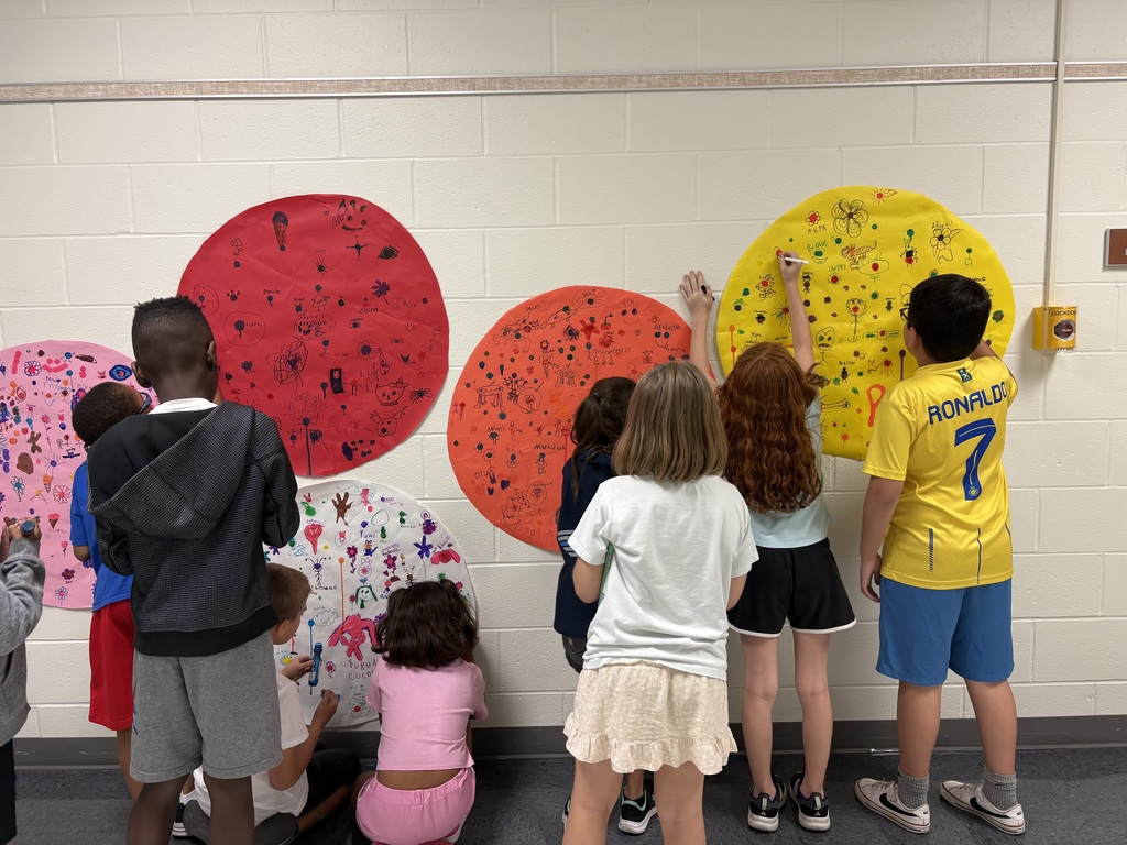 Seven students are drawing on a circular shaped paper in a hallway. 