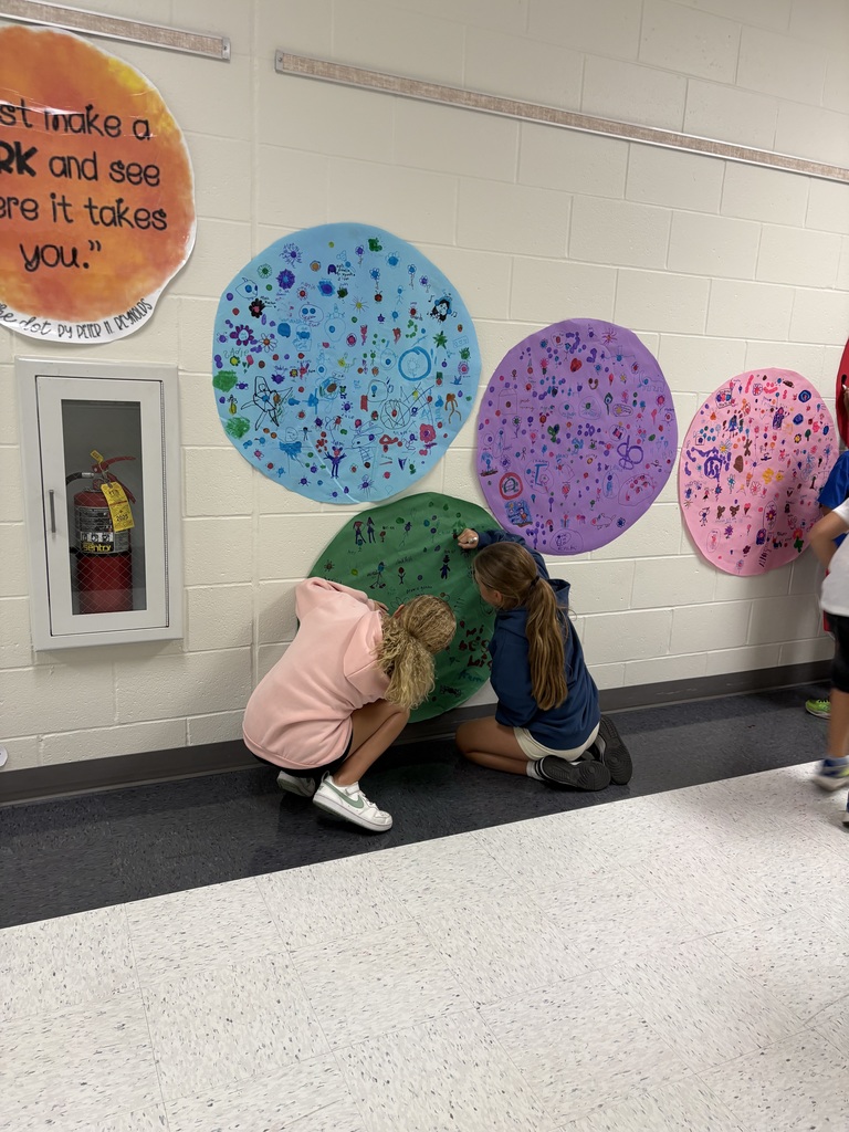 Two students are drawing on a circular shaped paper in a hallway. 