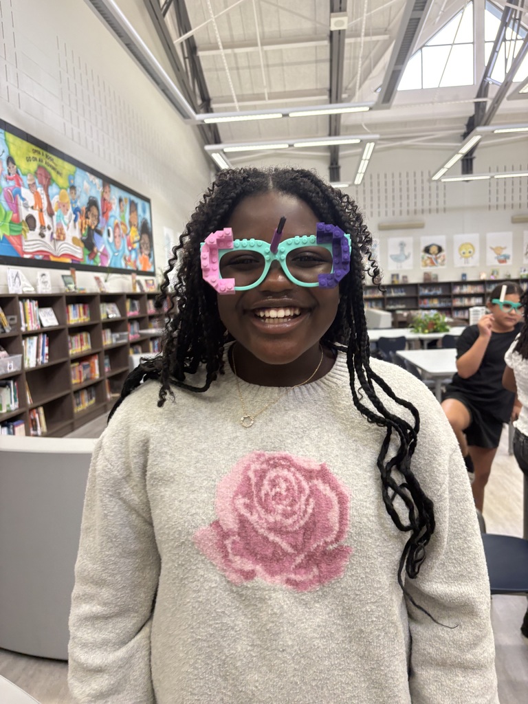 A student standing in the library wearing Lego glasses. 