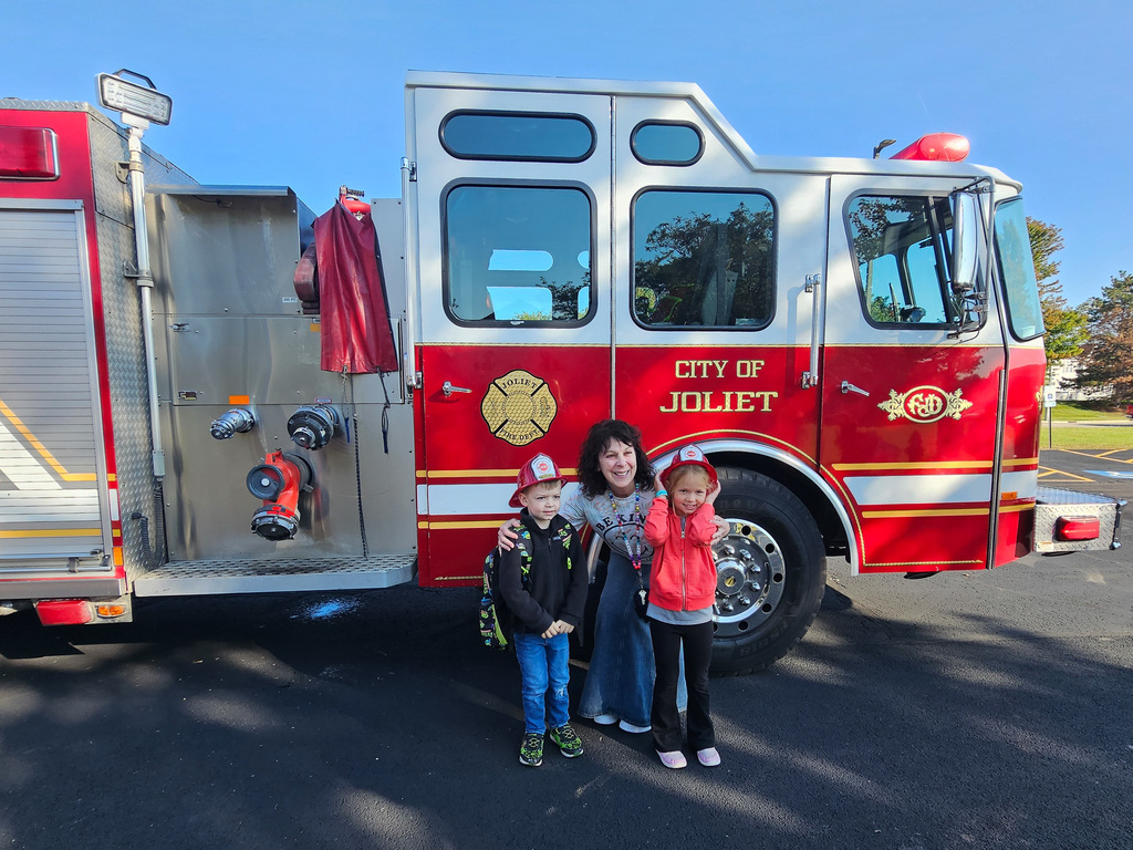 two students and teacher stand in front of red Joliet Fire Department fire truck