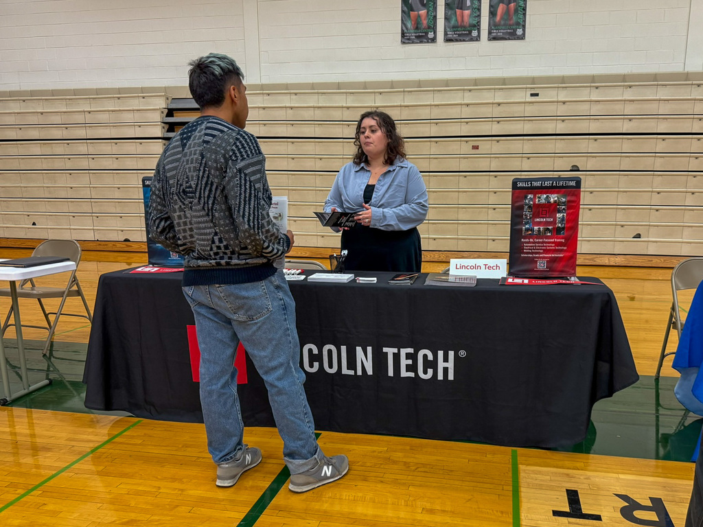 group of adults and students stand around employers tables in gym