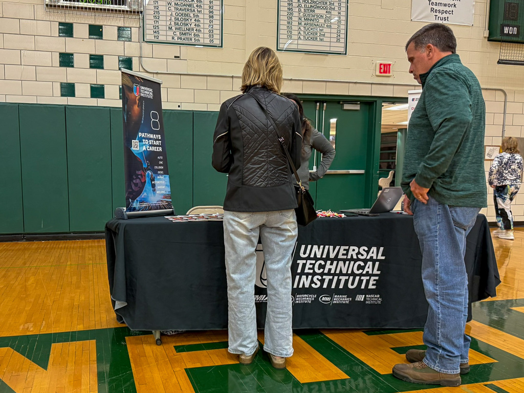 group of adults and students stand around employers tables in gym