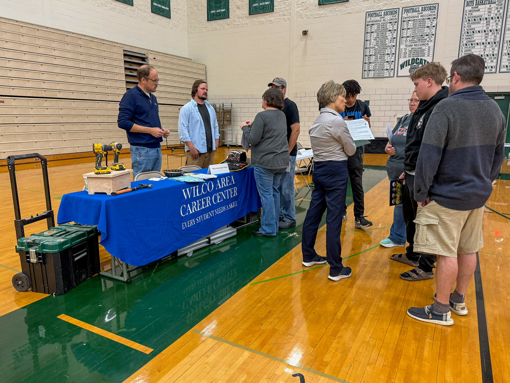 group of adults and students stand around employers tables in gym