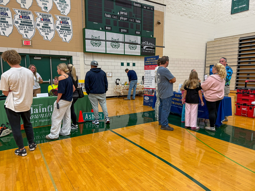 group of adults and students stand around employers tables in gym