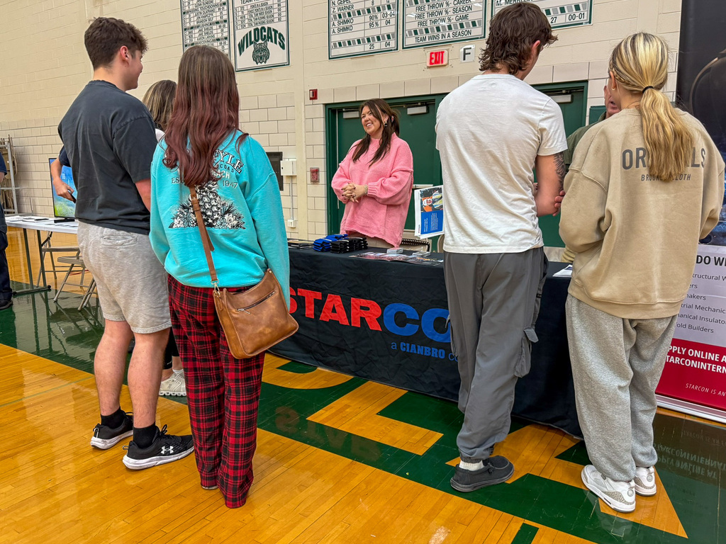 group of adults and students stand around employers tables in gym