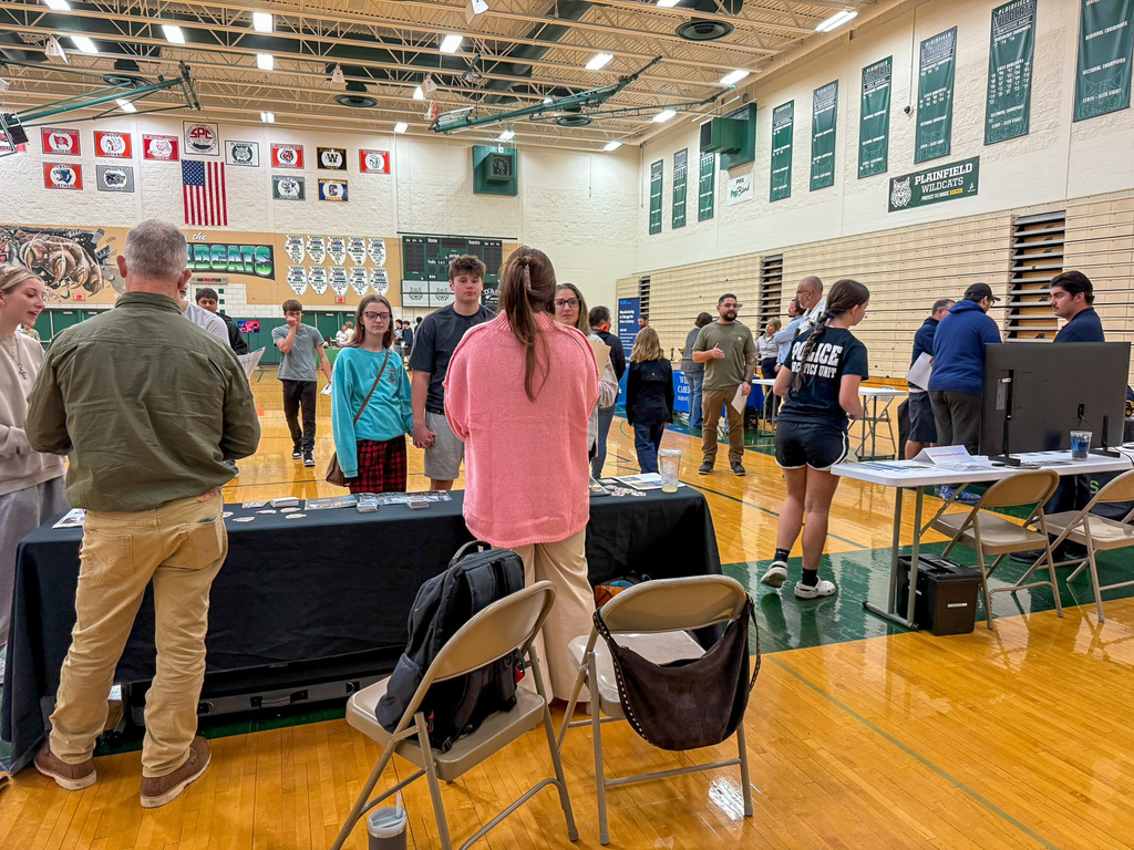 group of adults and students stand around employers tables in gym