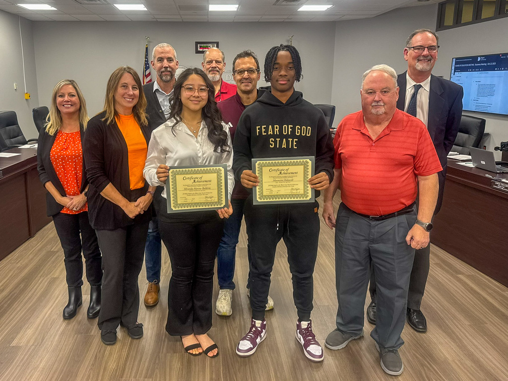 Board of Education stands with two high school students holding certificates