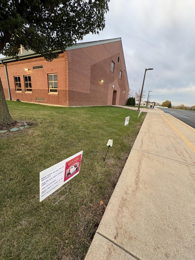 Signs with books pages in the grass in front of a school.