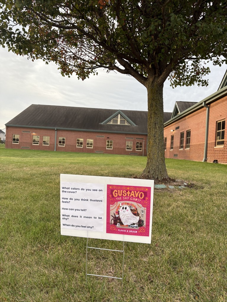 A sign with a book cover and questions is in the grass.
