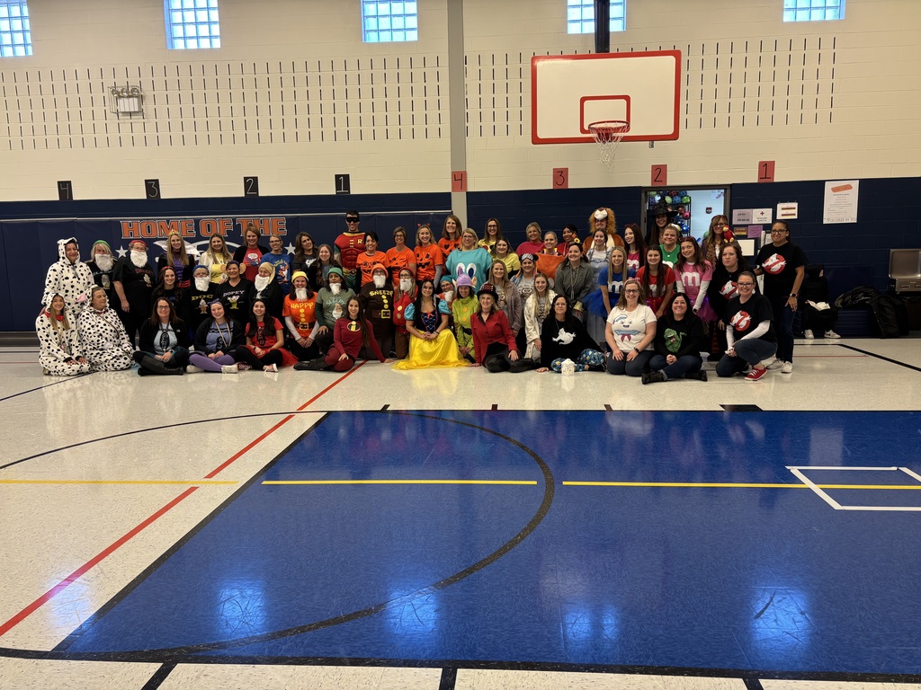 A large group of teachers in Halloween costumes standing in a gym.