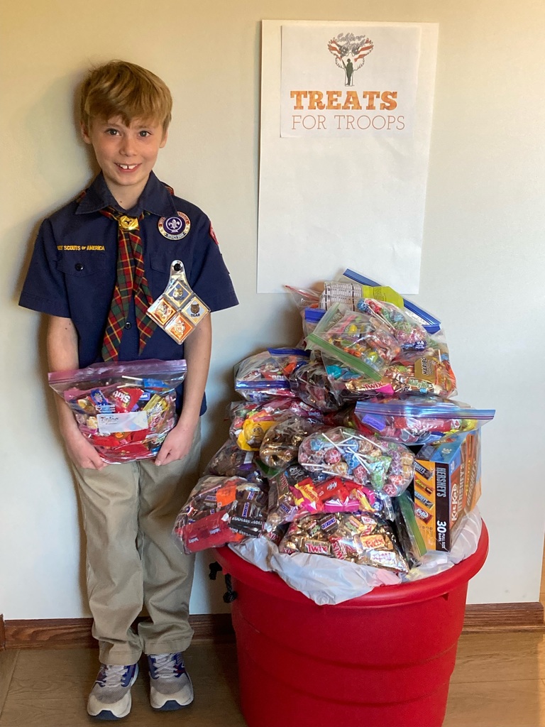 Boy Scout stand next  to a  red bucket filled with candy