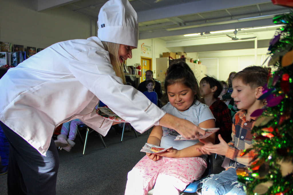 adult dressed in chef's coat hands cookies to students